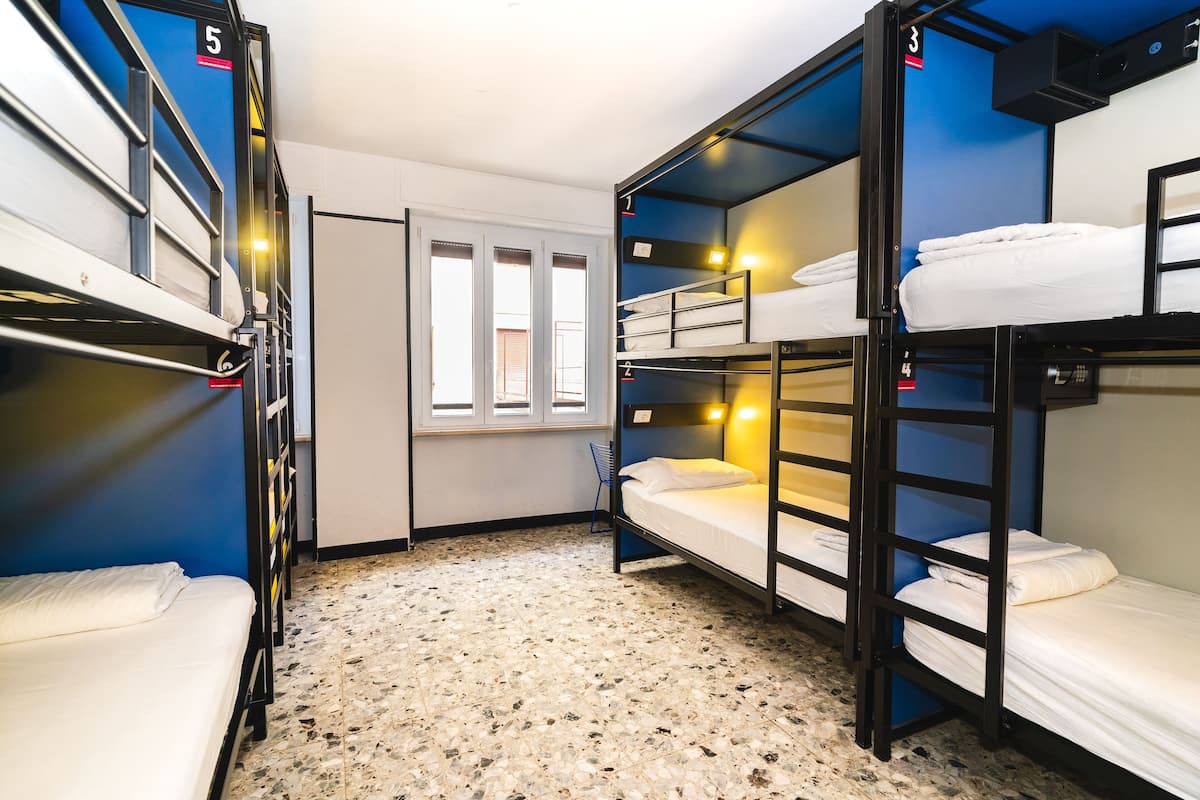 A dormitory room with bunk beds, numbered beds, a window, and a tiled floor.