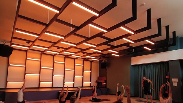 A yoga class in a room with wooden floors and a high ceiling with geometric light fixtures. - YellowSquare Milan (Milan)