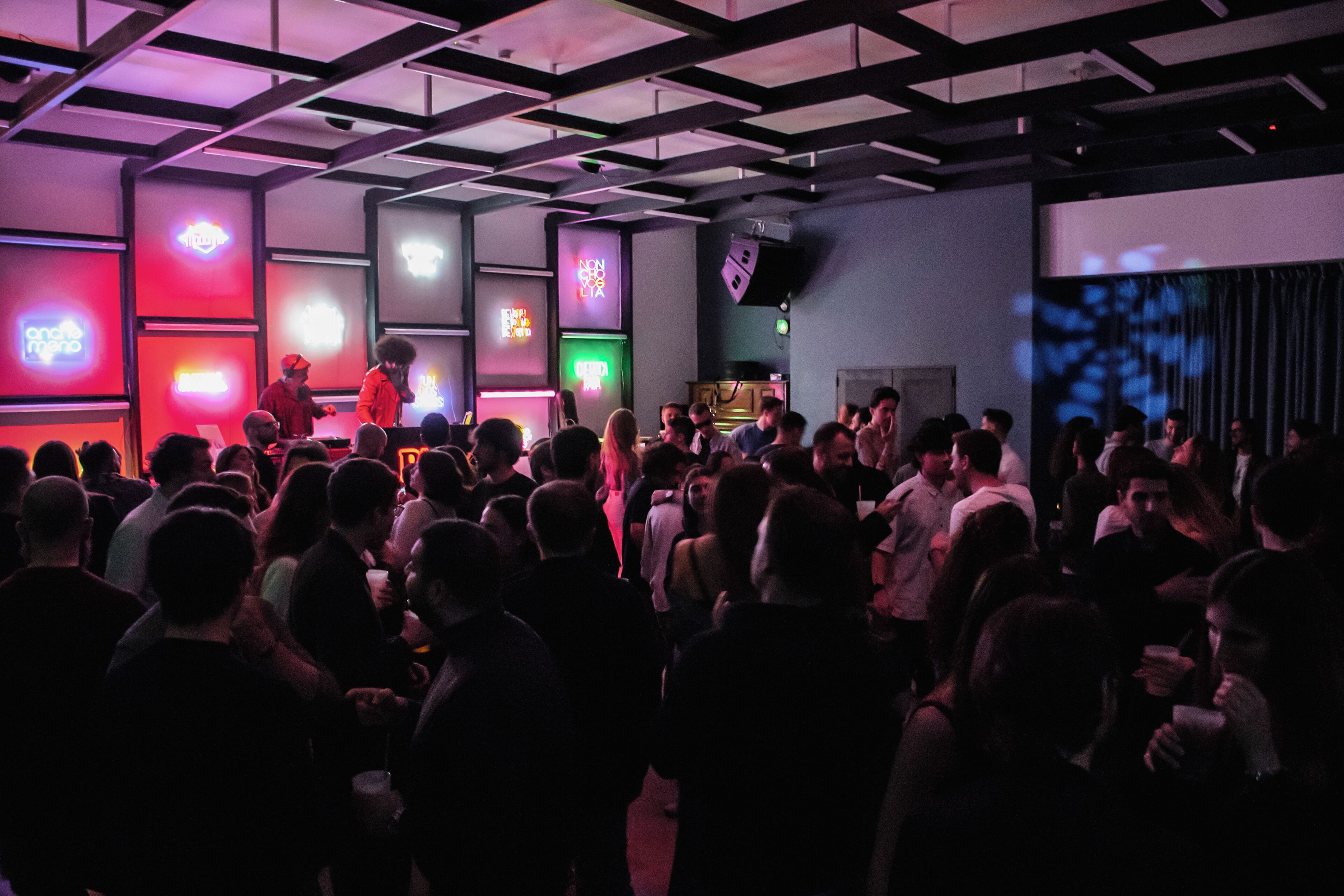 A crowded indoor event with a stage and neon signs.