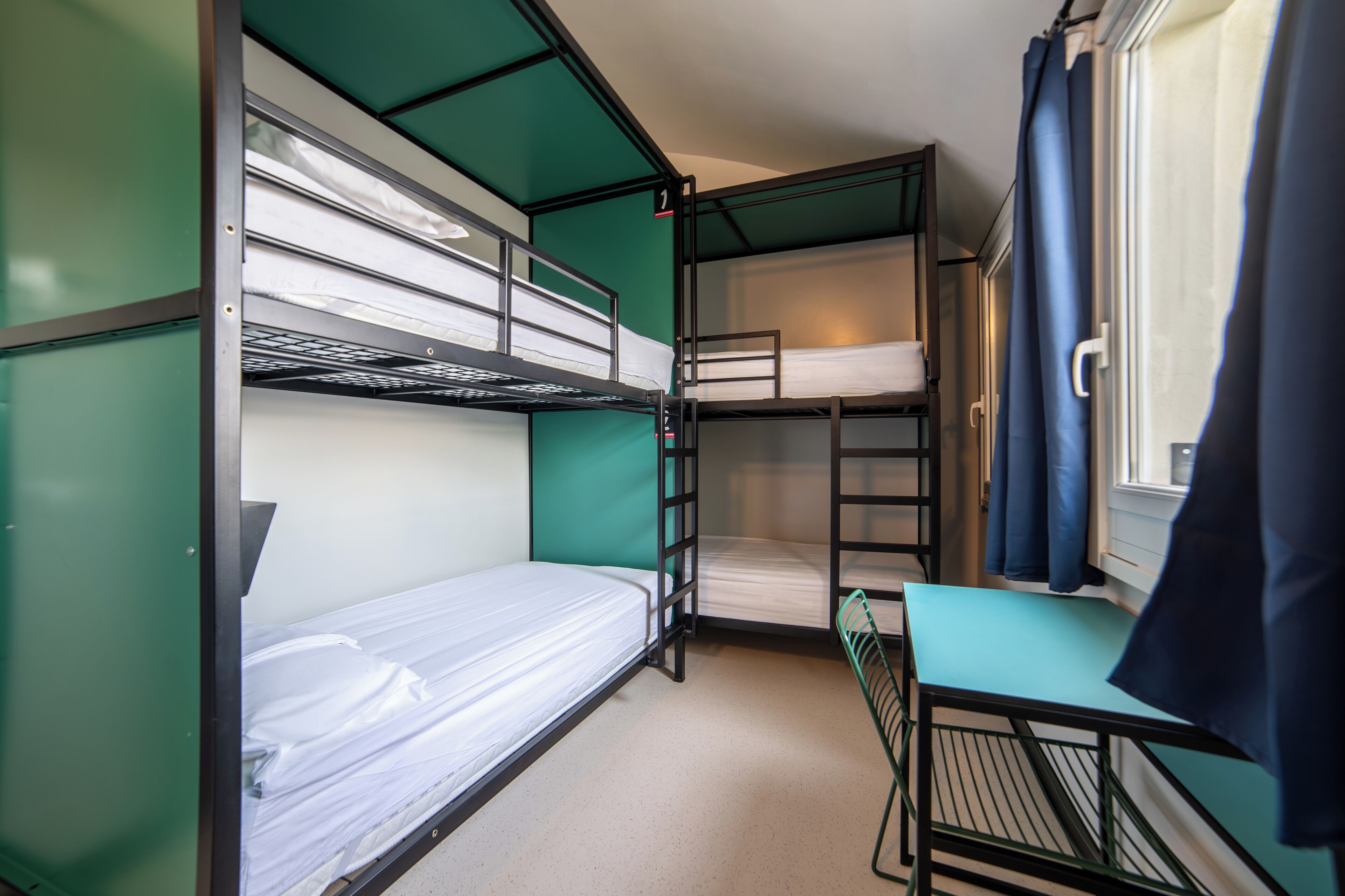 A bunk bed room with a desk and a window with curtains.