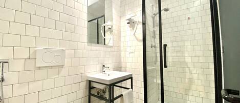 Bagno con pareti piastrellate di bianco, doccia vetrata, lavandino bianco e specchio.