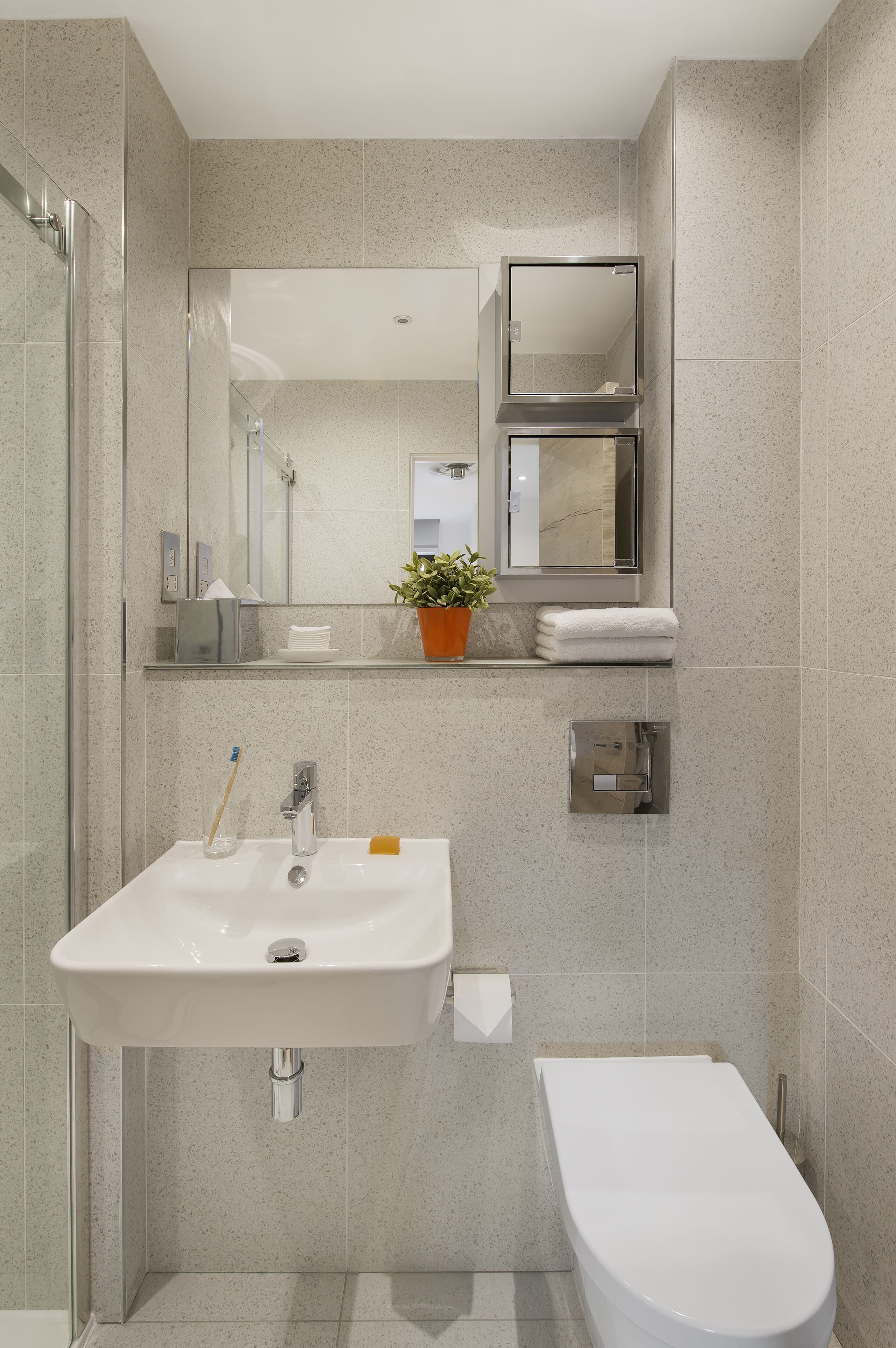 Une salle de bain moderne avec un lavabo blanc, des toilettes, une douche en verre et un miroir au-dessus du lavabo.