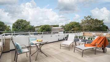 A rooftop terrace with outdoor seating, a table with fruits, and a view of the cityscape.