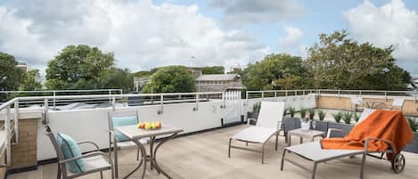 A rooftop terrace with outdoor seating, a table with fruits, and a view of the cityscape.
