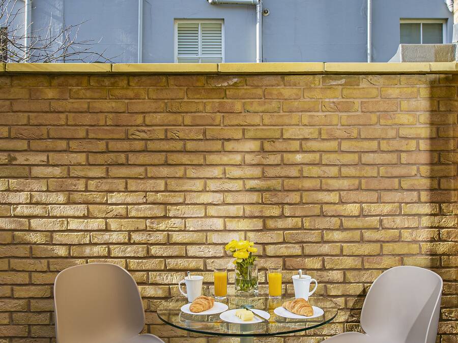 A patio with two chairs and a table, a brick wall, and a building in the background.