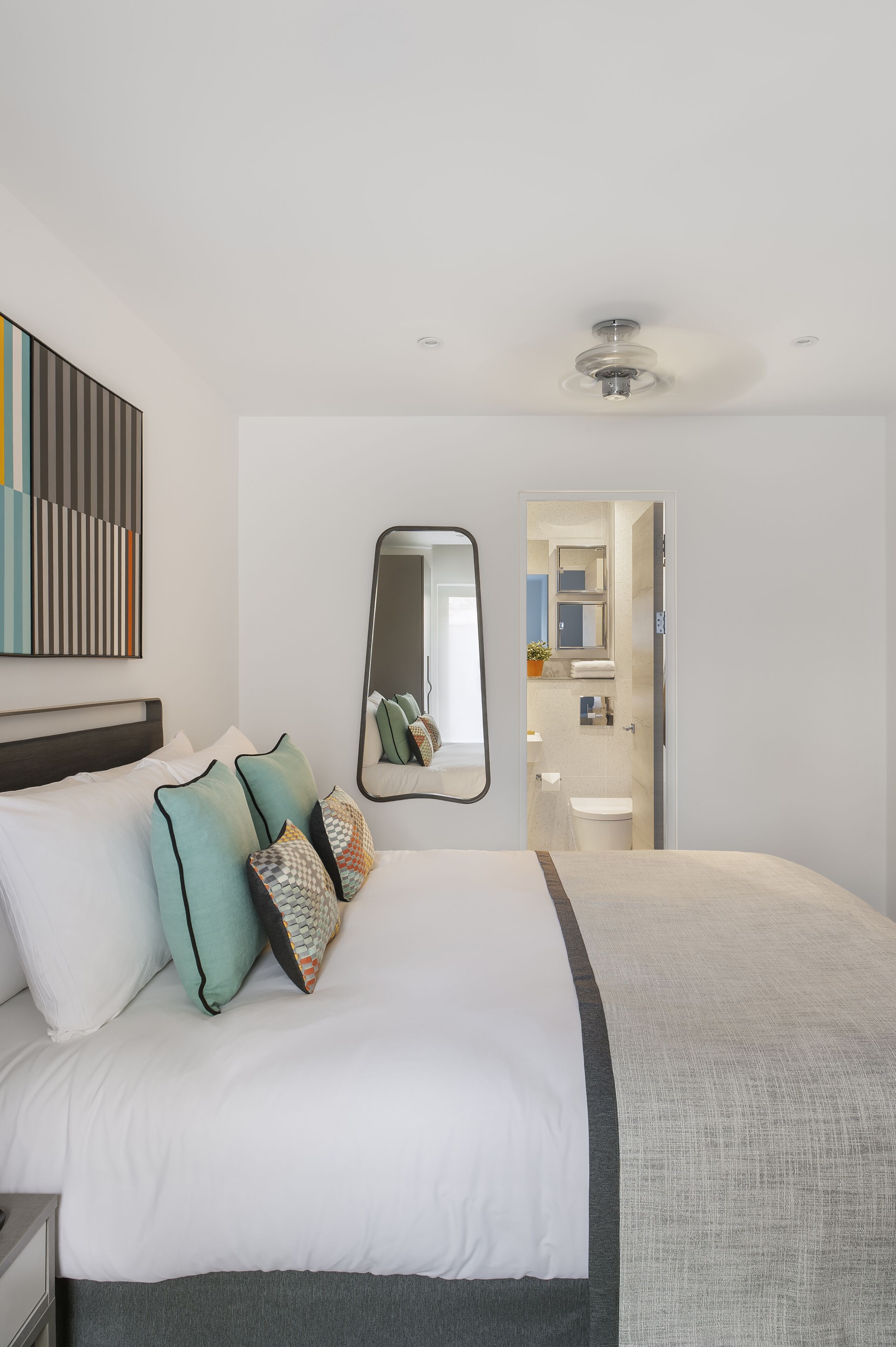 Et moderne hotelværelse med en stor seng, ventilator, spejl og udsigt til badeværelset.