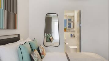 A modern hotel room with a large bed, a ceiling fan, a mirror, and a view into the bathroom.