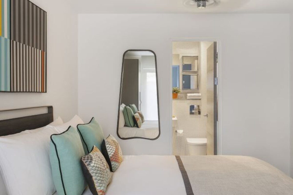 Habitación de hotel con cama, almohadas, un espejo y vistas al baño.