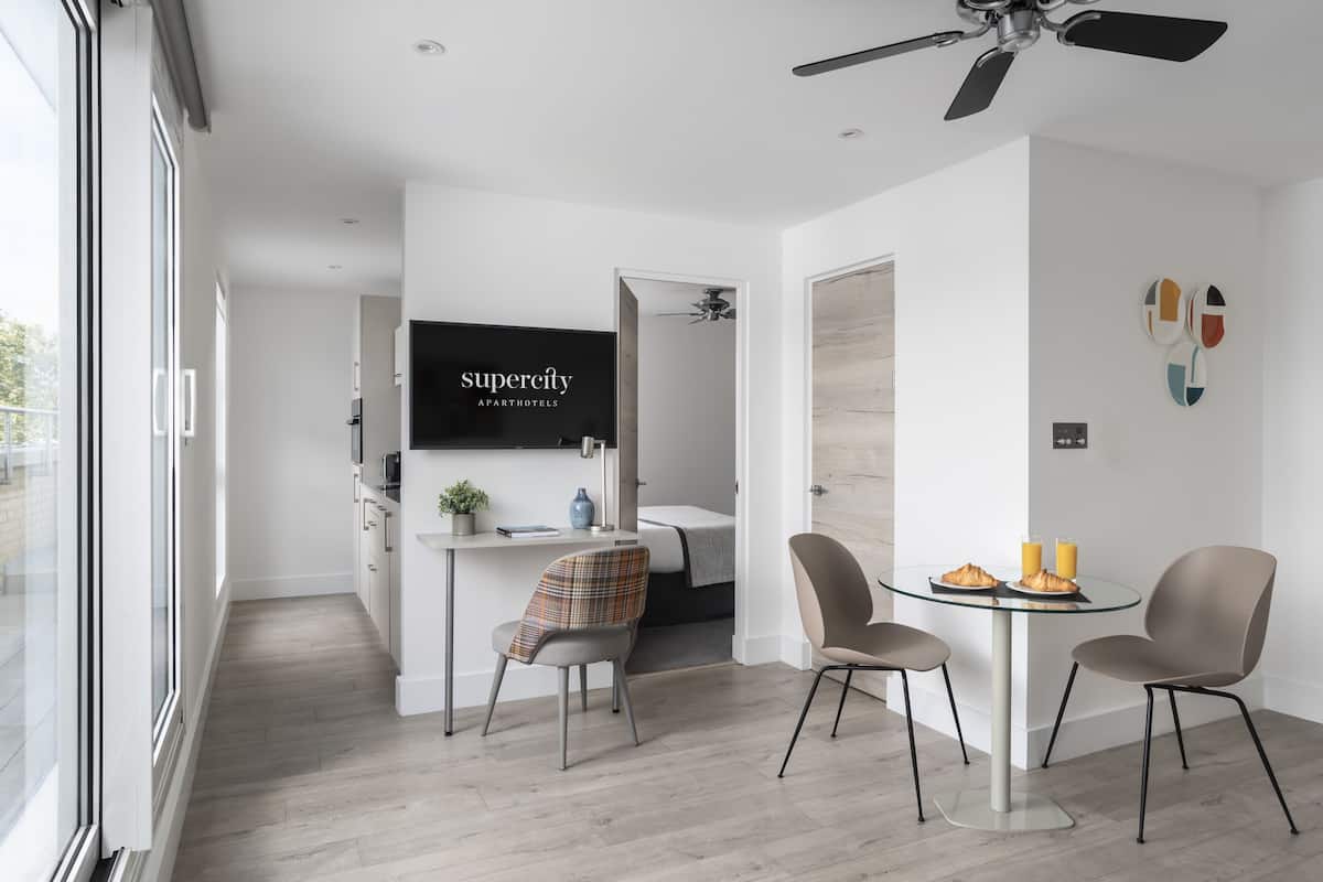 Een moderne keuken met een eetgedeelte, een plafondventilator en een televisie waarop 'superecity apartments' wordt weergegeven.