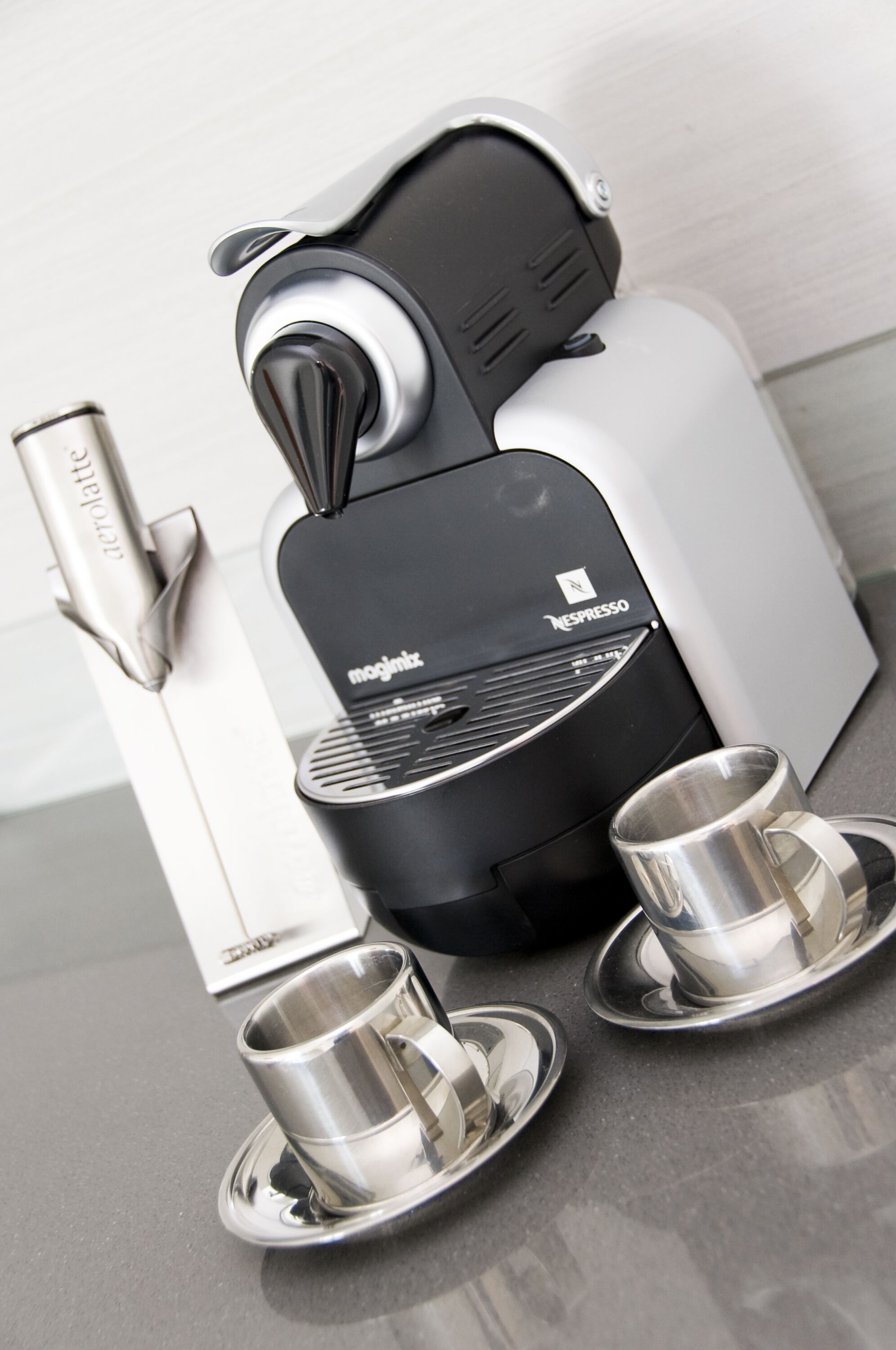 A Nespresso coffee machine with two stainless steel cups on saucers.