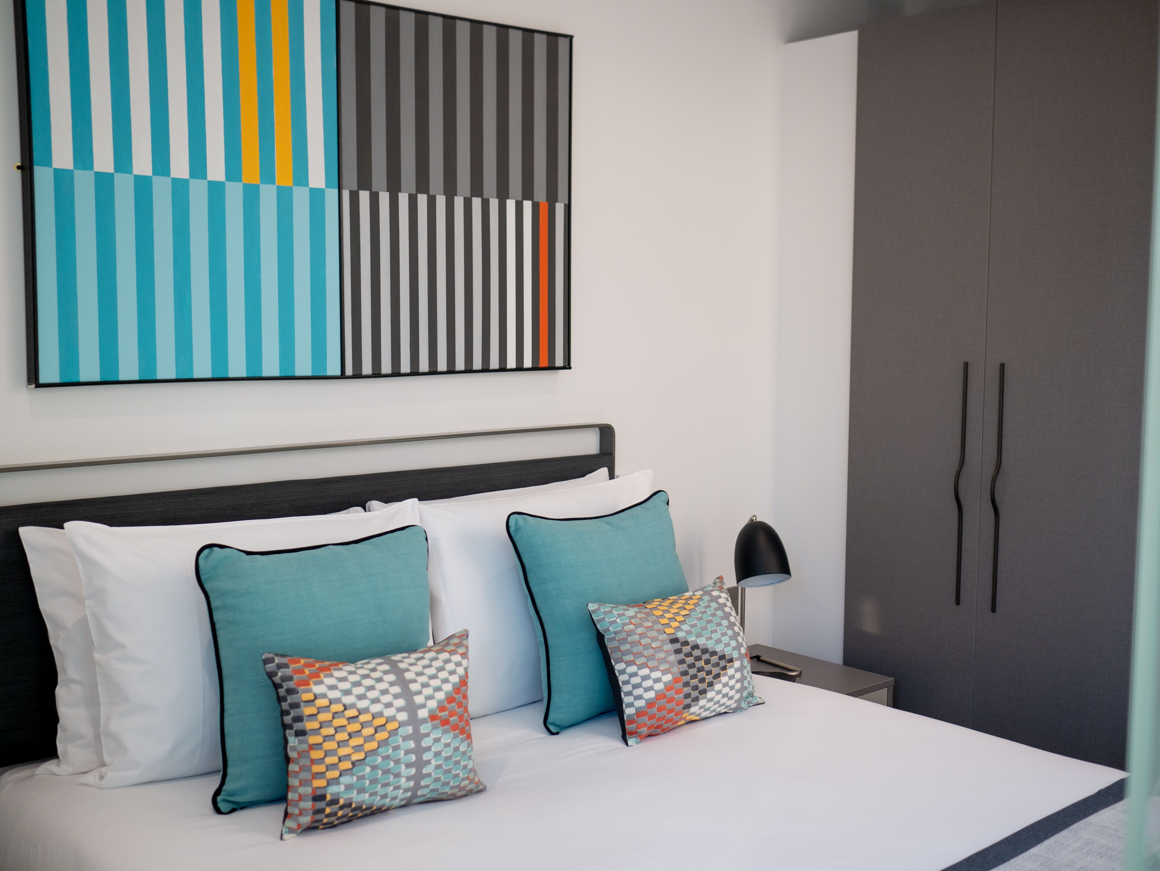 A modern bedroom with a bed, pillows, a nightstand, a lamp, and a wardrobe.