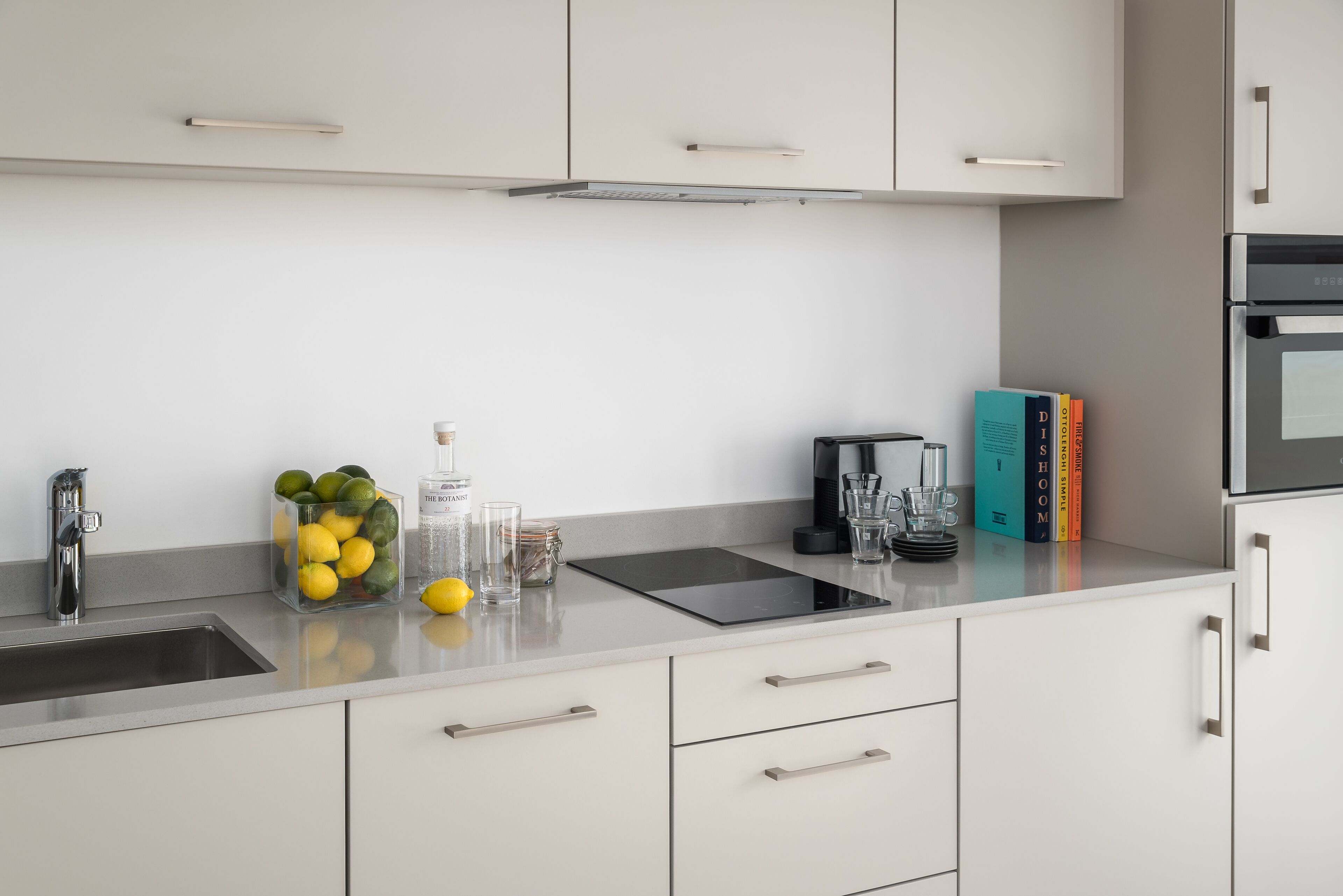 Een moderne keuken met witte kastjes, een roestvrijstalen spoelbak en een aanrecht met een glazen pot vol citroenen en een koffiezetapparaat.