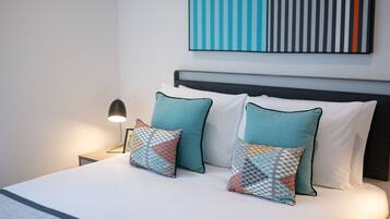 A neatly made bed with two patterned pillows, a bedside lamp, and a modern abstract painting on the wall.