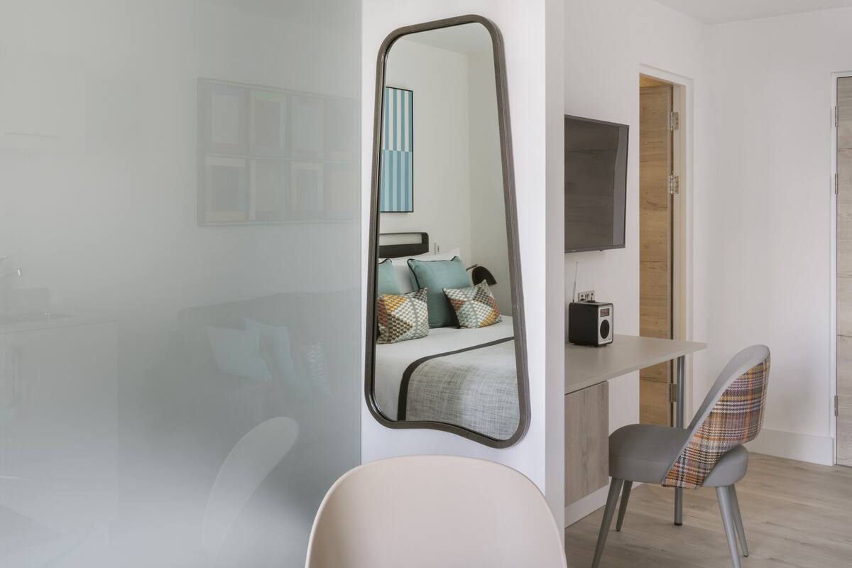 Een moderne kamer met een glazen eettafel, een stoel, een bank, een televisie en een spiegel.