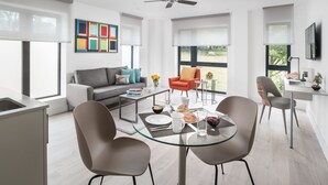 A modern living room with a glass dining table, grey sofa, and a ceiling fan.