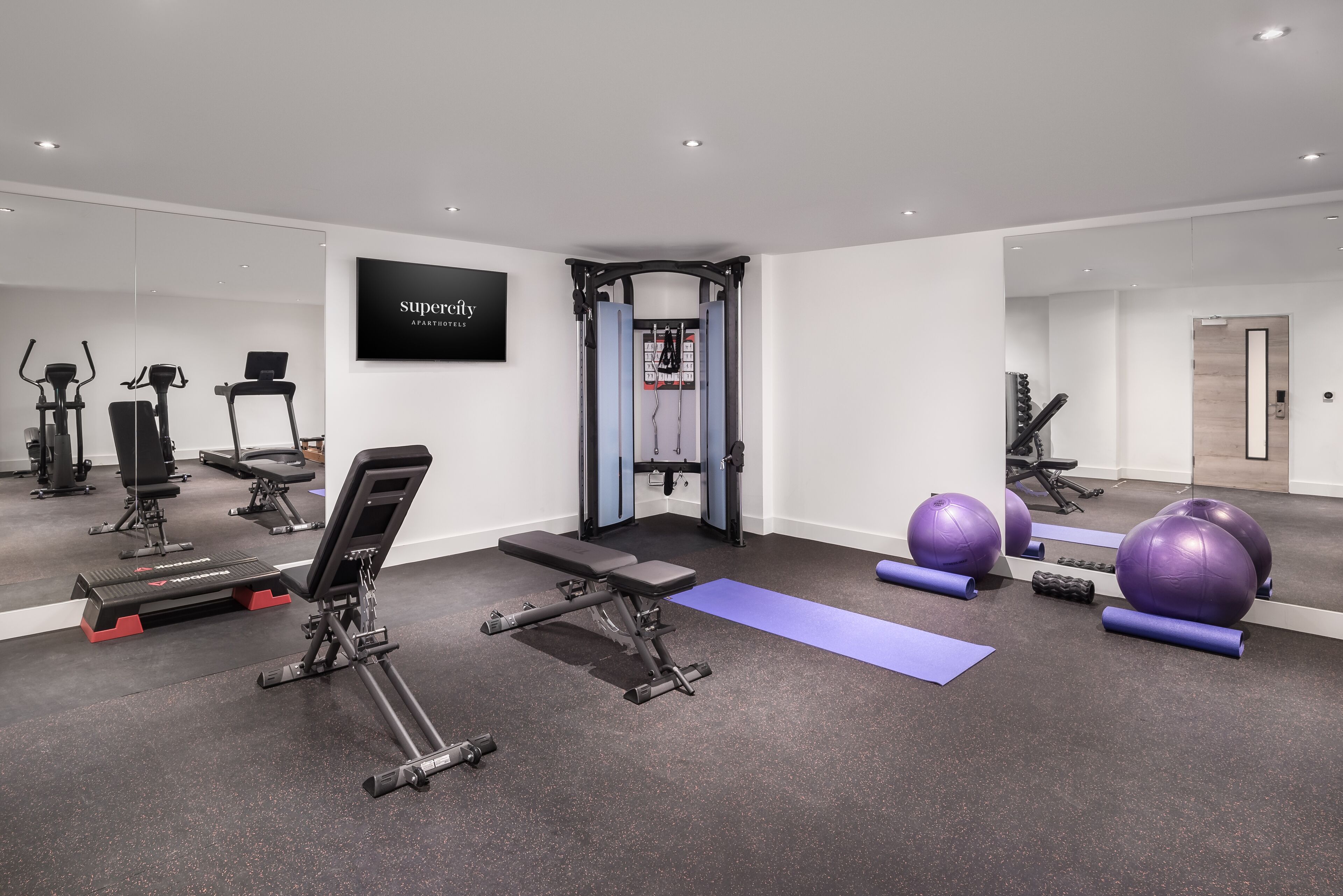 Uma academia moderna com diversos equipamentos de exercício, incluindo esteiras, um banco e bolas de ginástica.