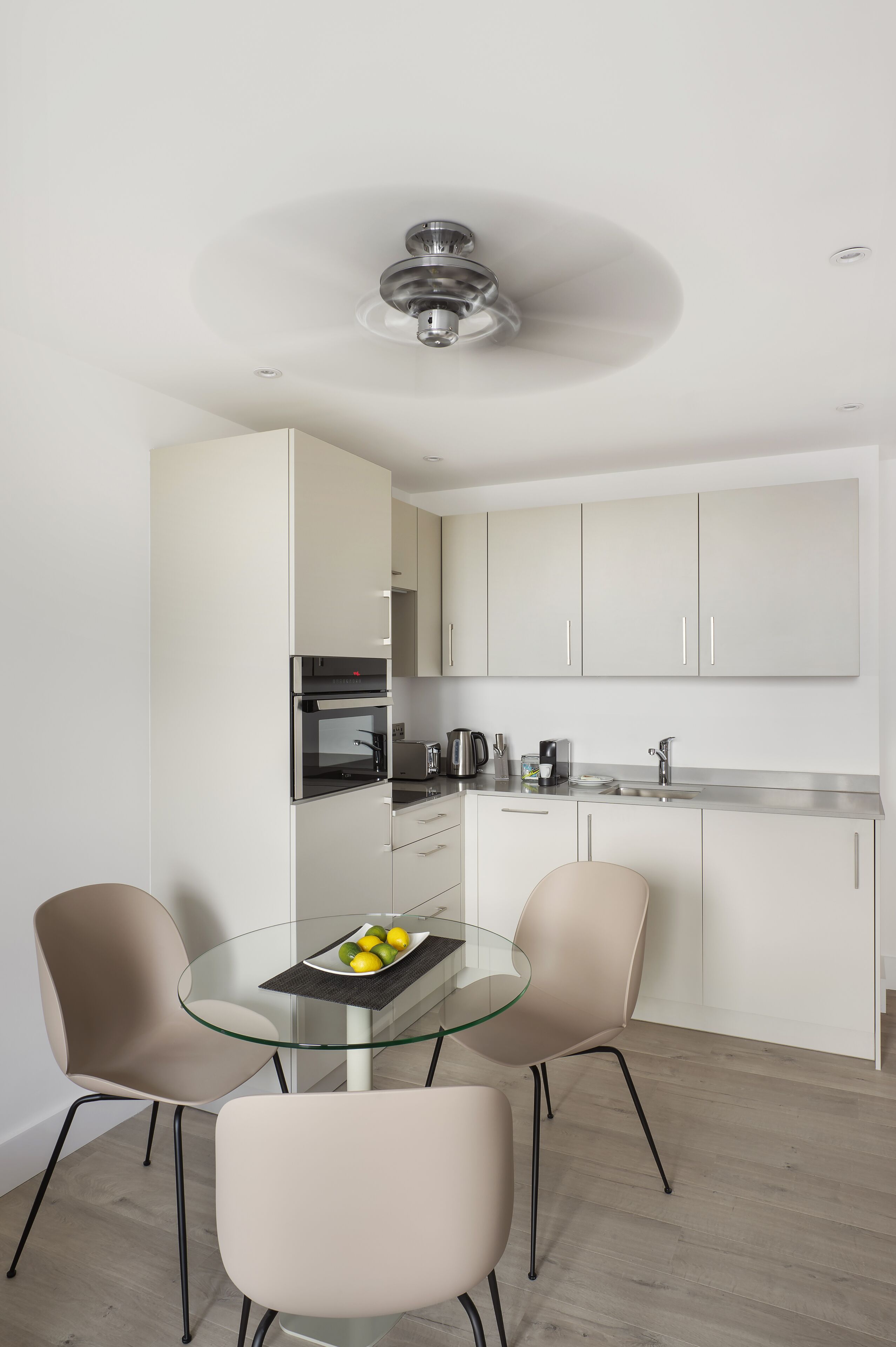 A modern kitchen with white cabinets, a glass dining table, and two chairs.