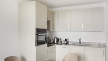 A modern kitchen with white cabinets, a glass dining table, and two chairs.