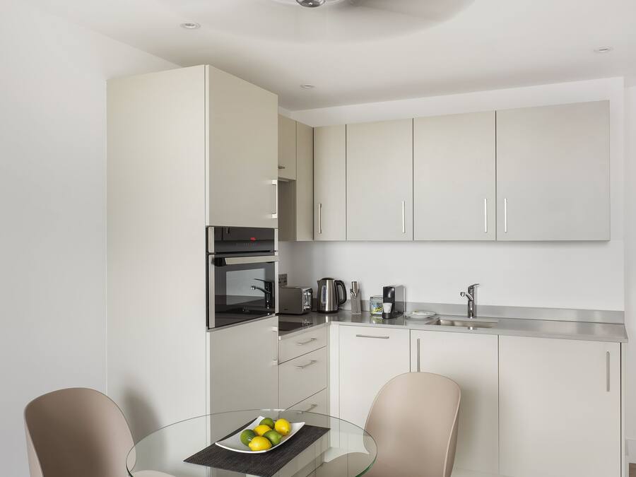 A modern kitchen with white cabinets, a glass dining table, and two chairs.