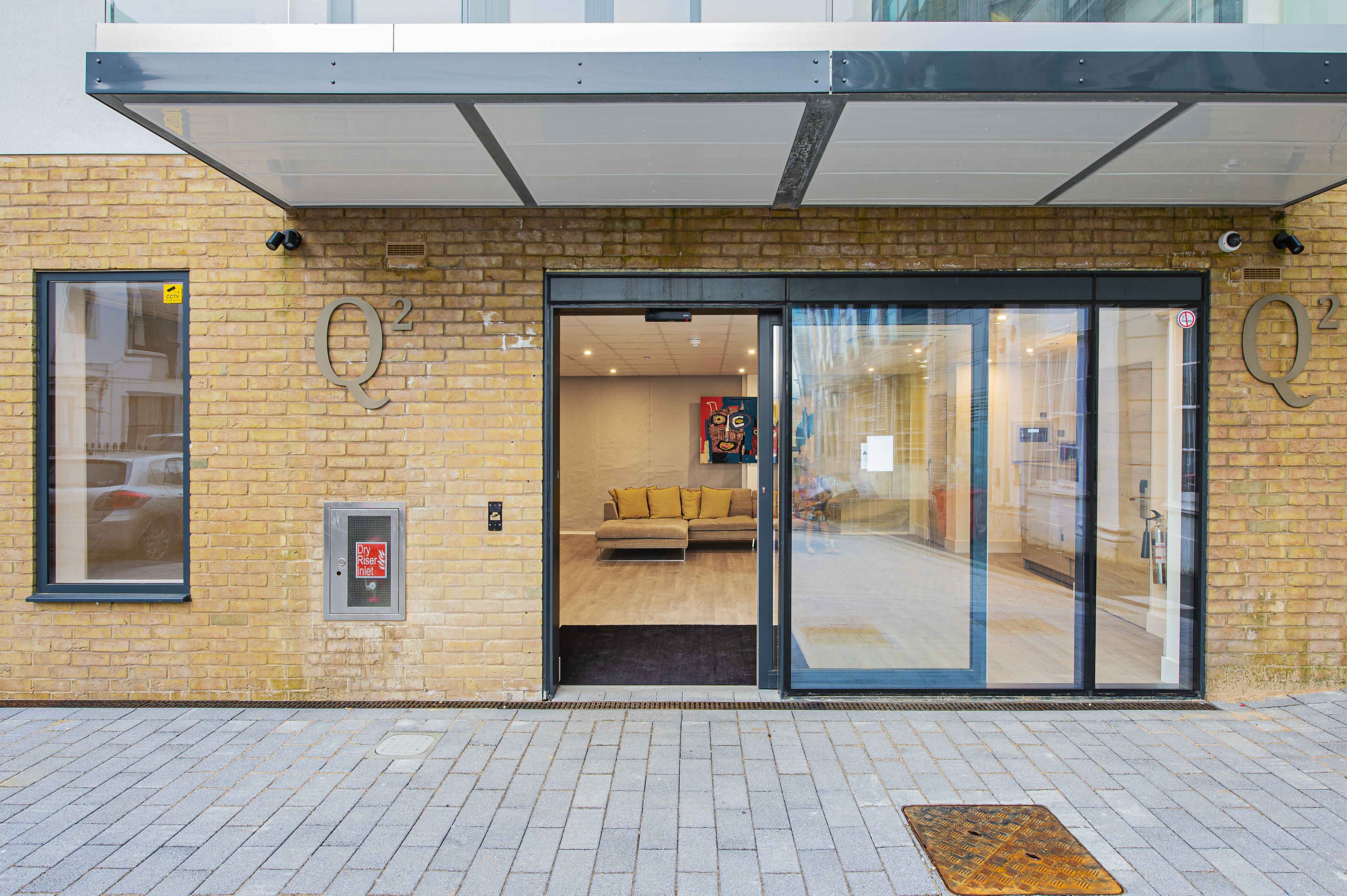 A hotel entrance with a glass door, a visible interior with a sofa and cushions, and a brick facade.