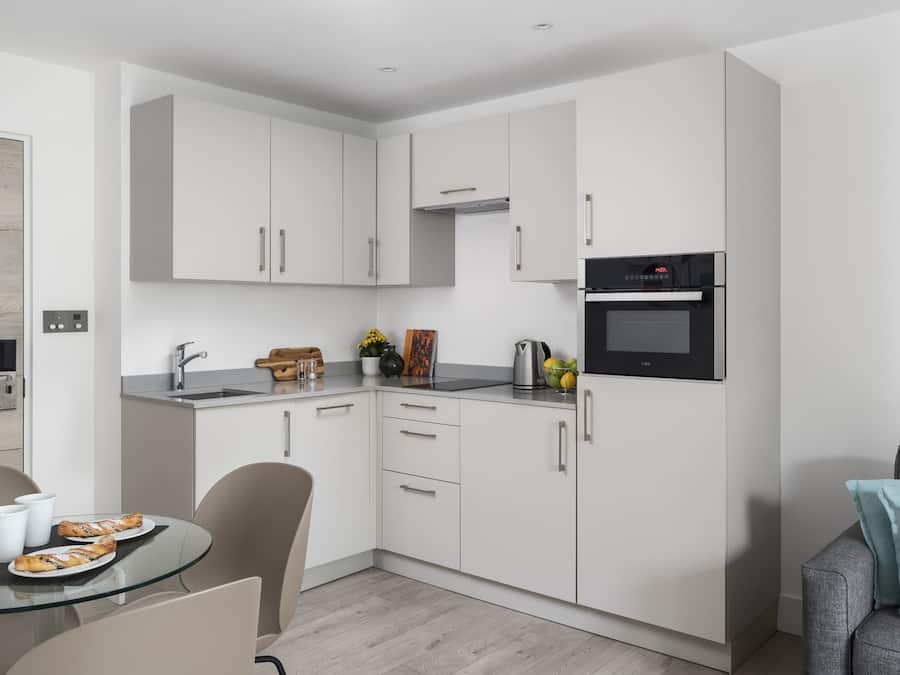 A modern kitchen with white cabinets, a stainless steel sink, and a built-in oven.