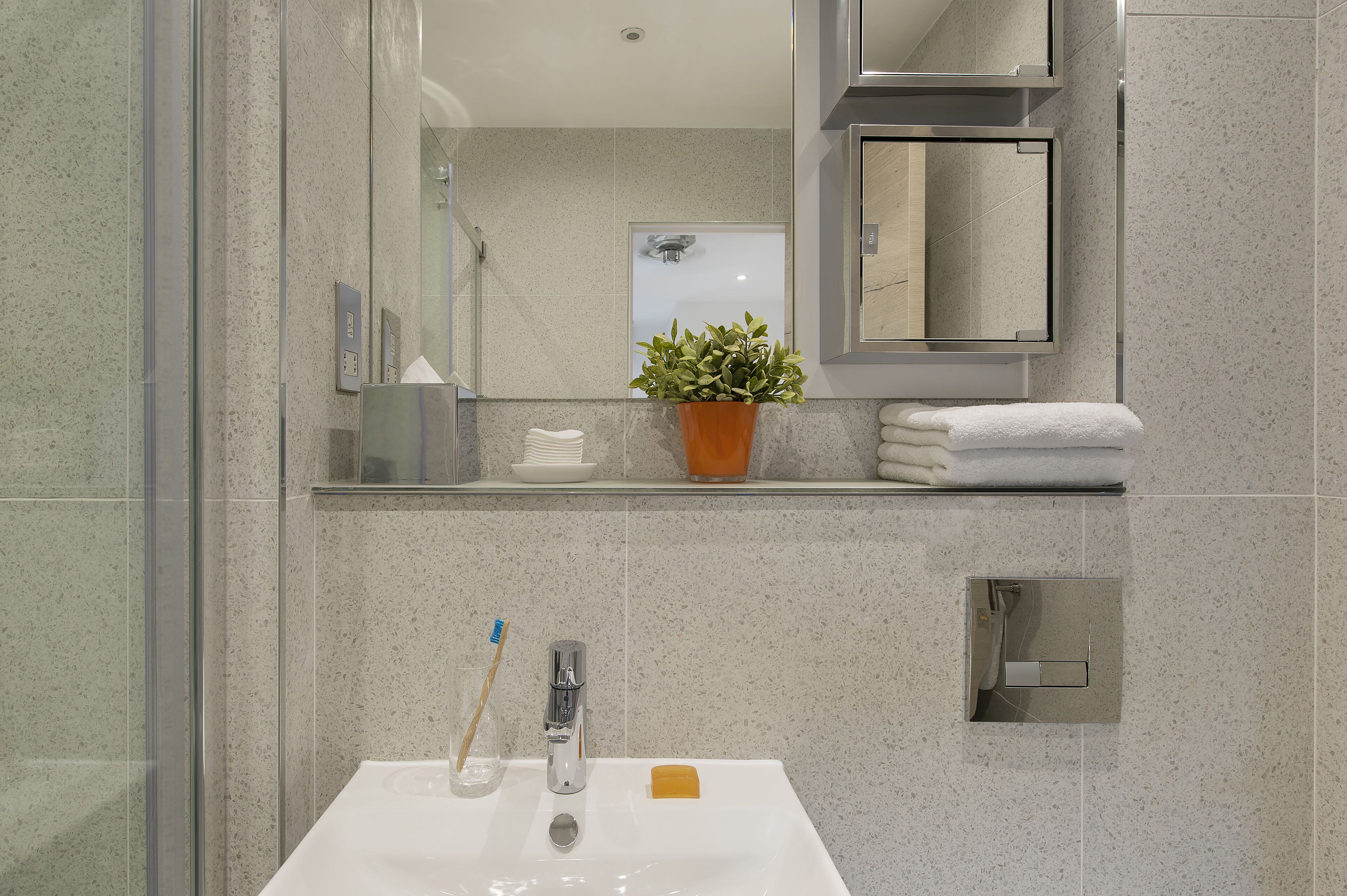A bathroom with a white sink, a glass shower enclosure, a potted plant, and a towel rack.
