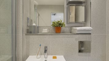 Een badkamer met een wit wastafelmeubel, een douchecabine met glazen wanden, een potplant en een handdoekhouder.