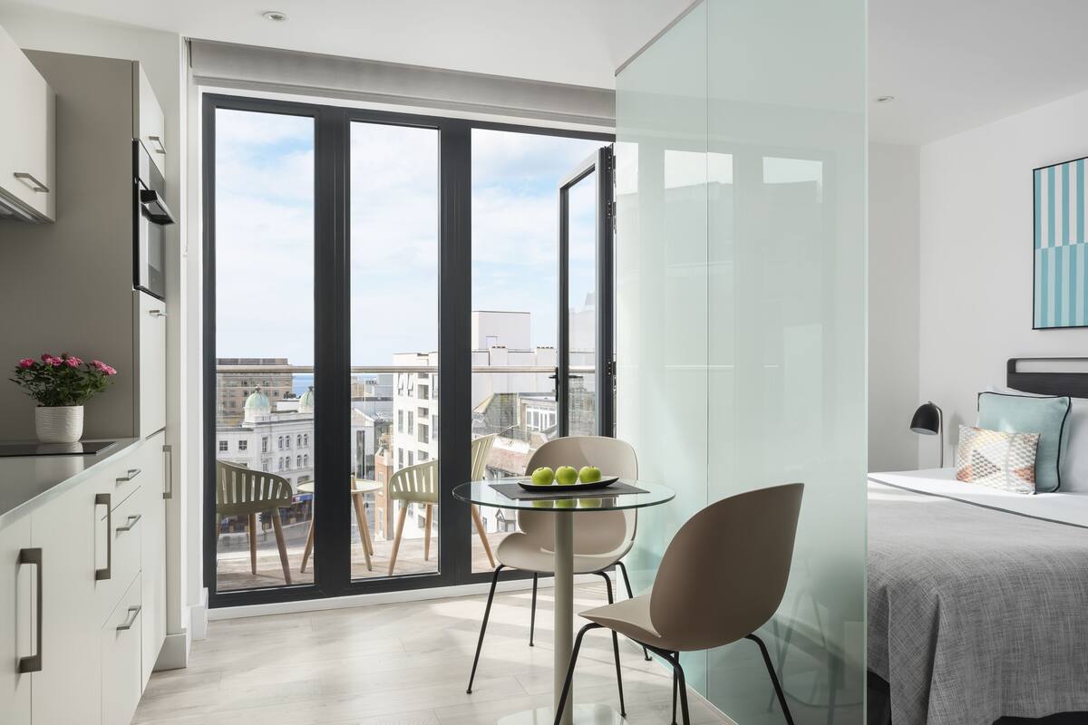 Een moderne hotelkamer met balkon, een zithoek met glazen tafel en een bed met uitzicht.
