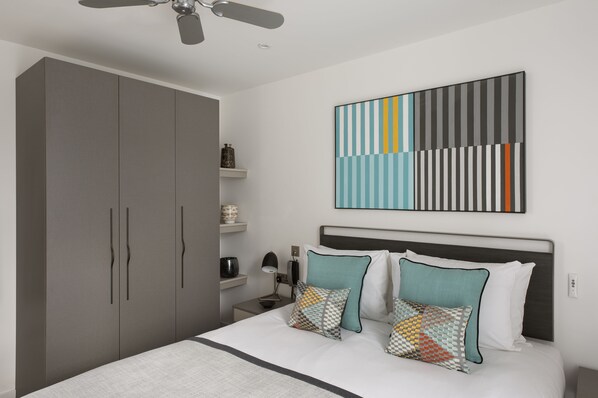 Un dormitorio moderno con una cama grande, un armario gris y un ventilador de techo.