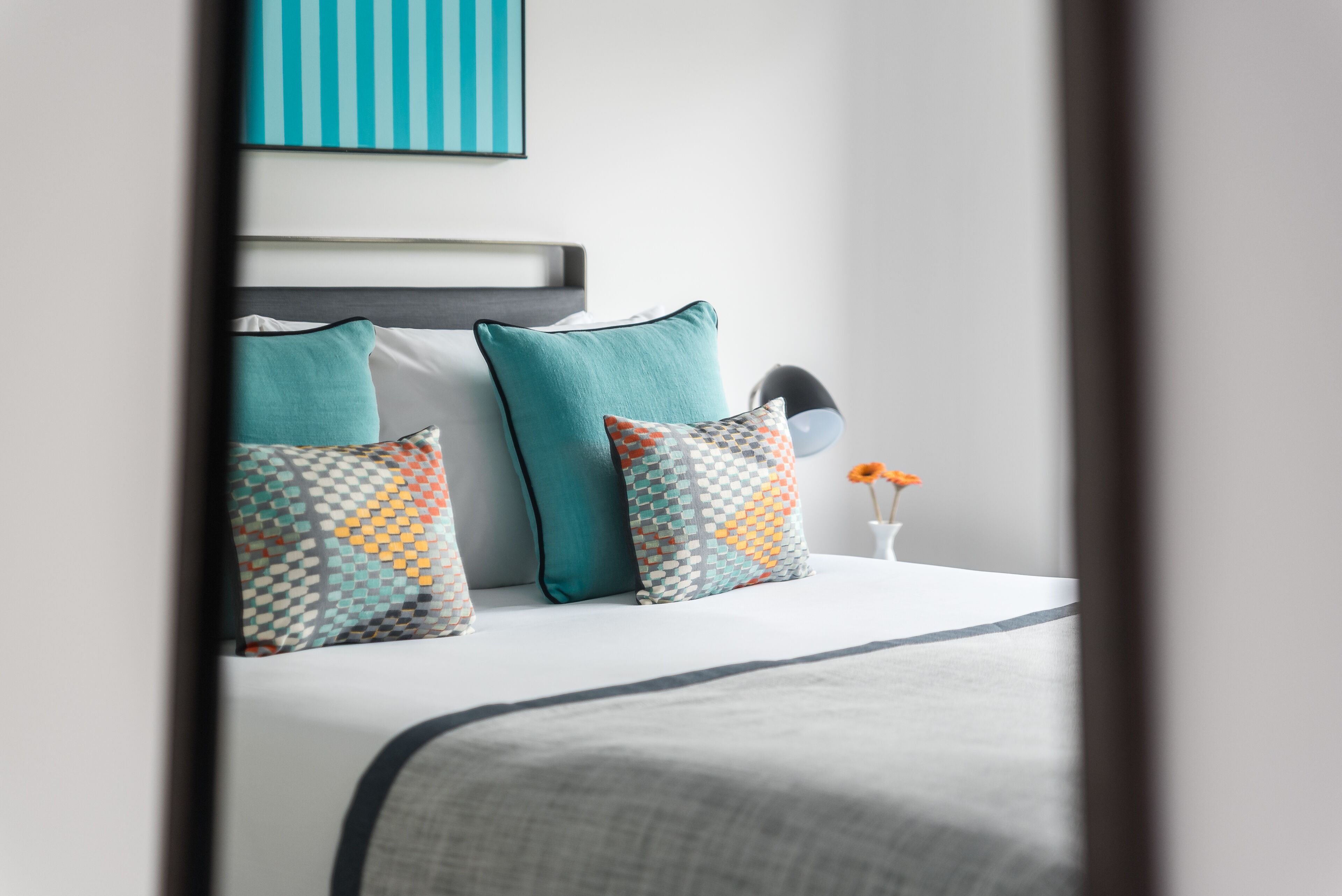 A neatly made bed with a grey bedspread and multiple pillows in various patterns.