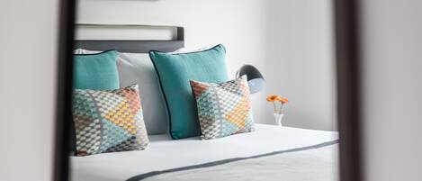 A neatly made bed with a grey bedspread and multiple pillows in various patterns.