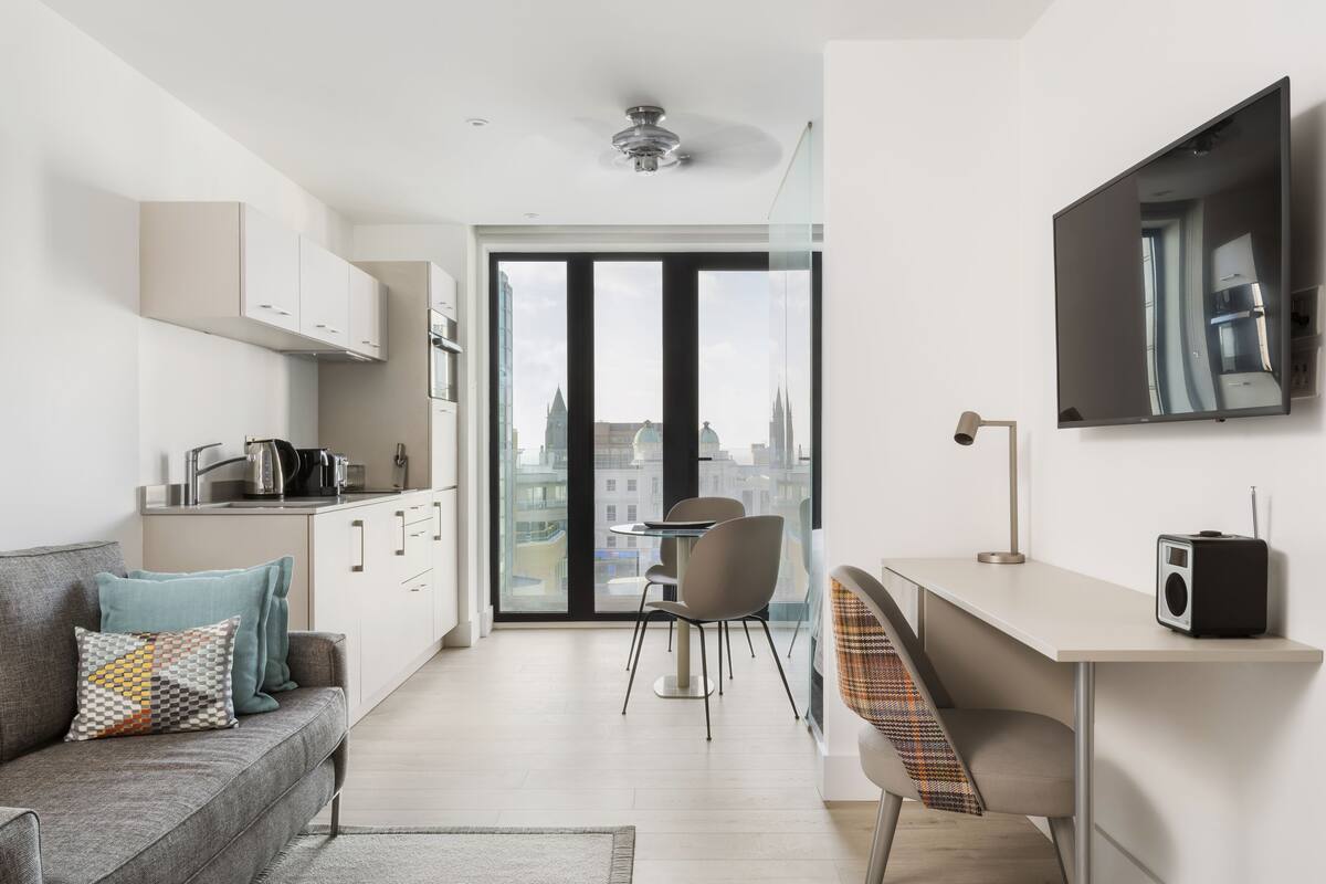 Een moderne, goed verlichte woonkamer met een bank, een eettafel en een keukenhoek.