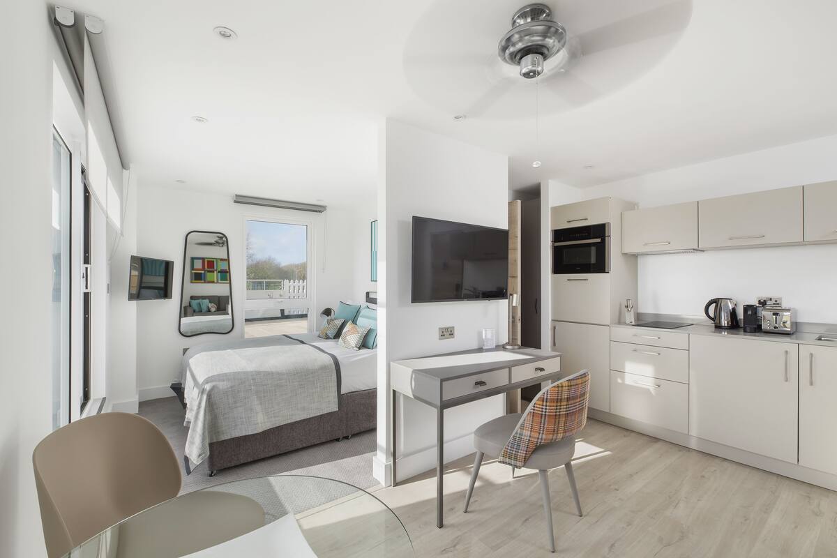 Een moderne, goed verlichte kamer met een bed, een bureau, een stoel en een kitchenette.