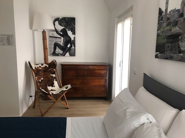 Une chambre à coucher comprenant un lit, une commode en bois, une chaise et deux œuvres d’art accrochées au mur.