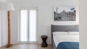 A bedroom with a bed, a floor lamp, a small stool, and a window with a view of historical architecture. - Roman Residenza : Bright, Quiet, and Modern in the Center of Rome (Roma)