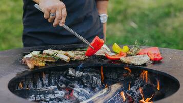 Una persona asando carnes y verduras en una parrilla al aire libre.