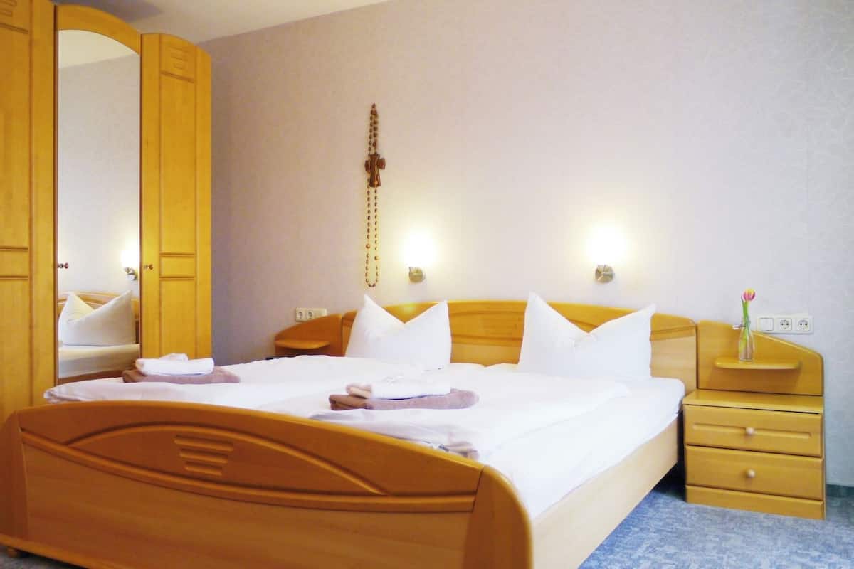 Habitación de hotel con cama de madera, almohadas blancas, mesita de noche con un florero y un espejo.