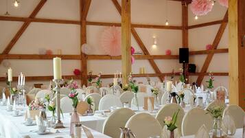 A banquet hall with wooden beams, white tables, and floral centerpieces.
