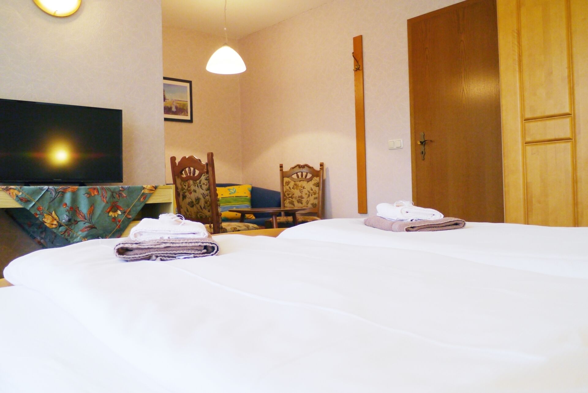 Ein Hotelzimmer mit zwei Betten, einem Fernseher, einer Holztür und einem kleinen Tisch mit Stühlen.