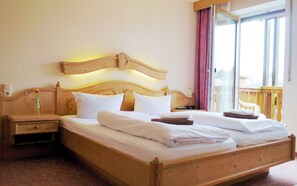A double bed with wooden headboard and headboard lamps, a nightstand with a vase, and a window with a view of a wooden deck. - Landgasthof Zum Hirschen (Kemnath)