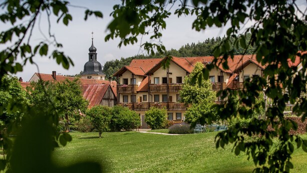 A hotel with a traditional architectural style, featuring a prominent church steeple and a well-maintained garden. - Landgasthof Zum Hirschen (Kemnath)