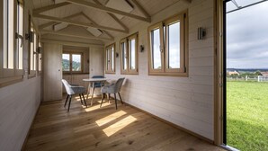 A spacious room with wooden floors and large windows, a table with chairs, and a view of a green landscape. - Landgasthof Zum Hirschen (Kemnath)