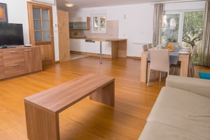 Uma sala de estar moderna com um banco de madeira, um sofá e uma área de jantar com mesa posta para quatro pessoas.