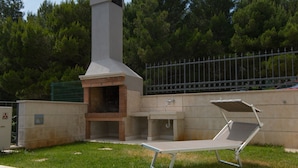 An outdoor kitchen area with a chimney, a grill, and a lounge chair. - Apartments Lumare with private pool (Pula)
