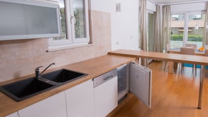 A modern kitchen with a double sink, dishwasher, and a dining area with a table and chairs. - Apartments Lumare with private pool (Pula)