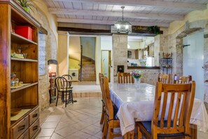 A rustic dining area with a wooden table and chairs, a chandelier, and stone walls. - Especially charm stone house with a pool (Marcana)