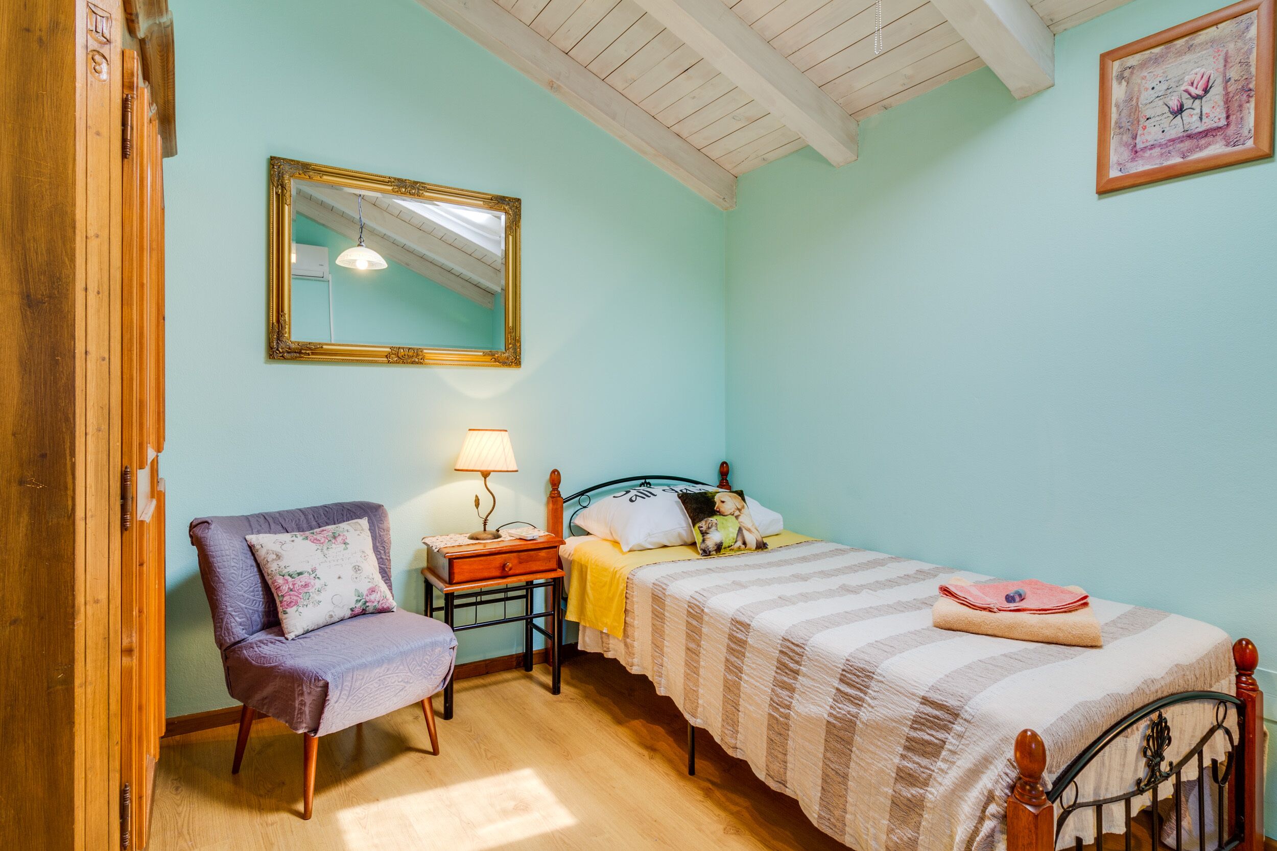 A bedroom with a bed, a chair, a nightstand, a lamp, and a mirror.