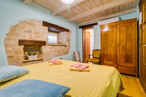 A bedroom with a stone wall, wooden ceiling beams, a bed with yellow bedding, a wooden wardrobe, and a small window with a plant. - Especially charm stone house with a pool (Marcana)