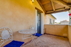 A covered outdoor seating area with a table and chairs, a door, and a view of buildings in the background. - Especially charm stone house with a pool (Marcana)