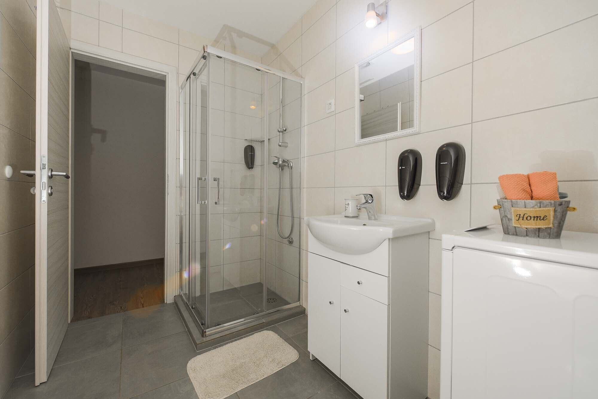 Ein modernes Badezimmer mit Duschkabine aus Glas, einem weißen Waschbecken und einer kompakten Ablage mit Handtüchern.
